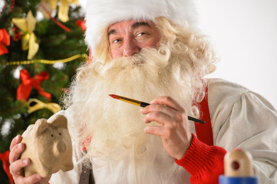 Authentic Santa Claus holding piggy bank and painting it