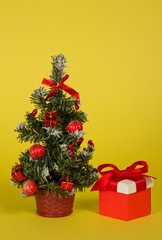 Fir-tree in a pot with toys and gifts on a yellow