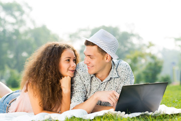 couple lying together in a park with laptop