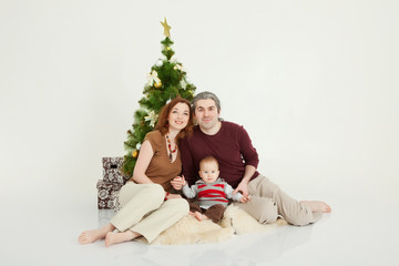 Happy family sitting at the new-year tree on white studio