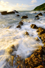 Obraz premium Ocean waves against rocks on the beach at sunset