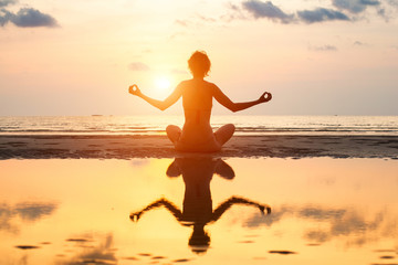 Yoga woman sitting in lotus pose on the beach during sunset.