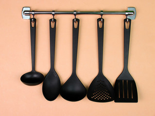 Black kitchen utensils on silver hooks, on peach background