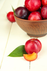 Ripe plums in bowl on wooden table close-up