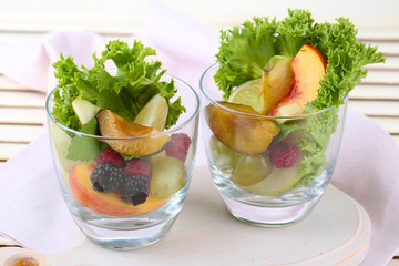 Fruit salad in glasses, on wooden background