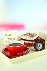 Cup of tea with cakes on wooden tray on table in room