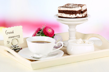 Cup of tea with cakes on wooden tray on table in room