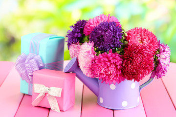 Gifts and flowers in watering can, on nature background