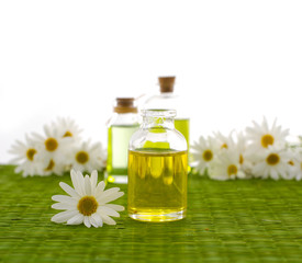 Obraz na płótnie Canvas Glass Bottle with daisy flowers, massage oil on green mat