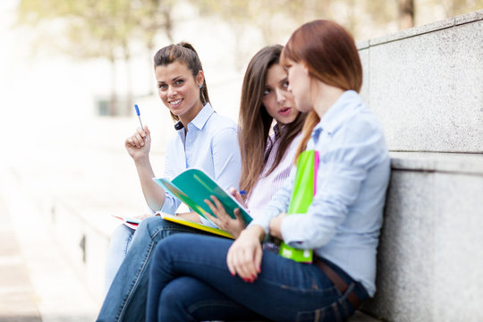 Three female students sitting on a bench with notebooks
