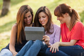 Three woman sitting on grass and looking at a digital tablet