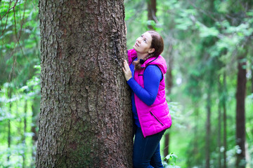 Attractive woman hugging big pine tree trunk in the forest