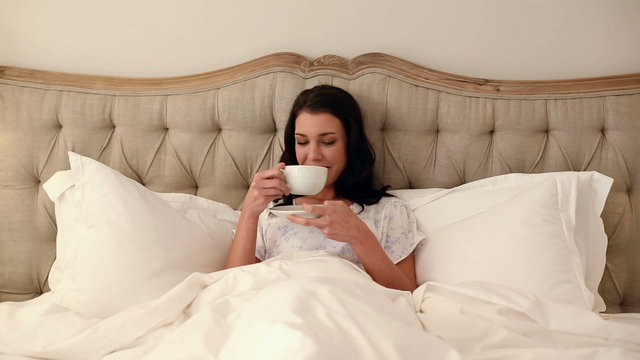 Beautiful brunette lying in bed drinking coffee