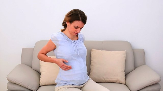Pregnant woman rubbing her painful neck on the couch