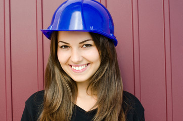 Girl on a construction site wearing a blue safety helmet.