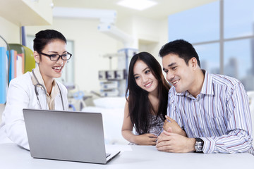 Obraz premium Female doctor looking a laptop with couple in clinic