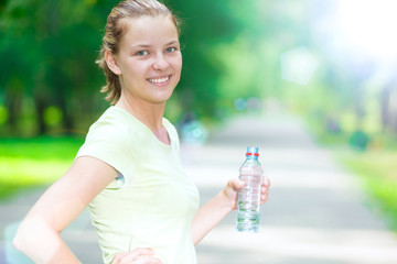 Woman drinking cold mineral water from a bottle after fitness ex