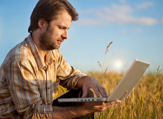 Modern farmer with laptop on his wheat field