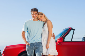 Smiling cute couple posing against their red cabriolet