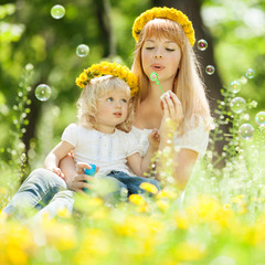 Obraz na płótnie Canvas Happy mother and daughter blowing bubbles in the park