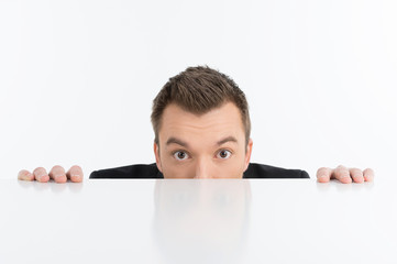 Scared businessman. Terrified young men looking out of the table