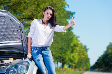 Beautiful woman hitchhiking by a broken car