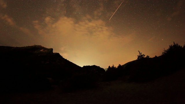 Time lapse of the night sky with clouds and stars passing by beh