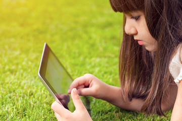 little girl lying on grass and touches the screen a tablet