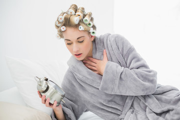 Stressed blonde woman in hair curlers looking at her alarm clock