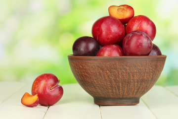 Ripe plums in bowl on wooden table on natural background