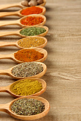 Assortment of spices in wooden spoons on wooden background
