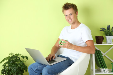 Young man relaxing with laptop in armchair,