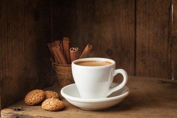 Coffee cup, Amaretti and Cinnamon sticks on wooden background