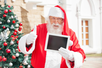 Santa Claus Gesturing Thumbsup While Holding Digital Tablet