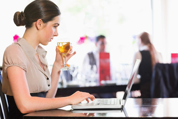 Attractive businesswoman holding wine glass while working on lap