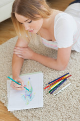 Happy young woman lying on floor sketching on paper