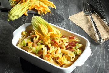 pasta con fiori di zucchino  e pancetta sfondo grigio