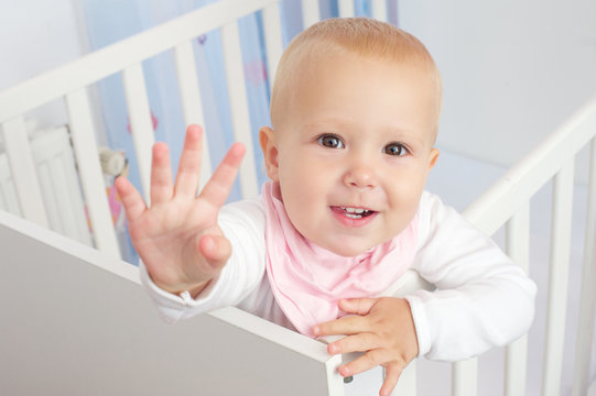 Portrait of a cute baby waving hello and smiling from crib