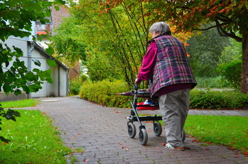 Frau, Seniorin schiebt Rollator auf Gehweg