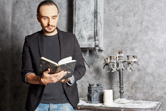 Young man stands reading book in room powdered with snow