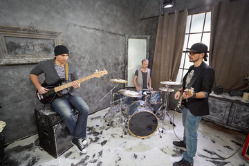 Two guitarists and drummer play in room powdered with snow