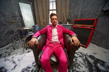 Young man in pink suit sits in dusk in old armchair