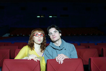 Young man and woman watch movie and surprise in cinema