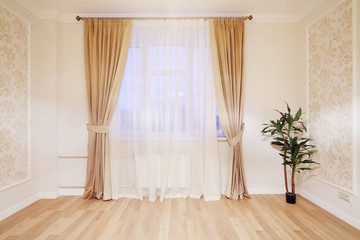 Window with beige curtains in simple room with plant on floor