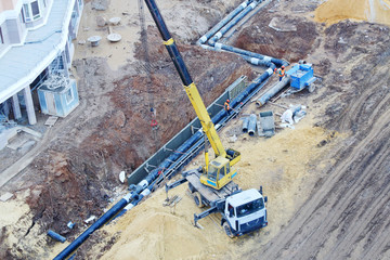 Truck Crane puts underground pipes at large construction site.