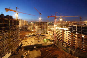 Lots of tower cranes build large residential buildings at night.