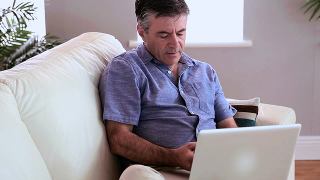 Mature man sitting using laptop and answering his phone
