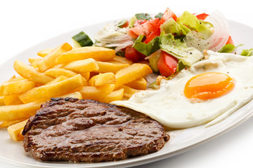 Grilled steaks, French fries, fried egg and vegetables