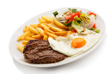 Grilled steaks, French fries, fried egg and vegetables