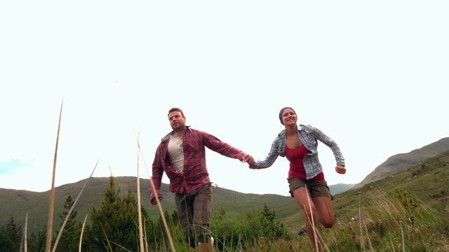 Happy couple running hand in hand though the countryside